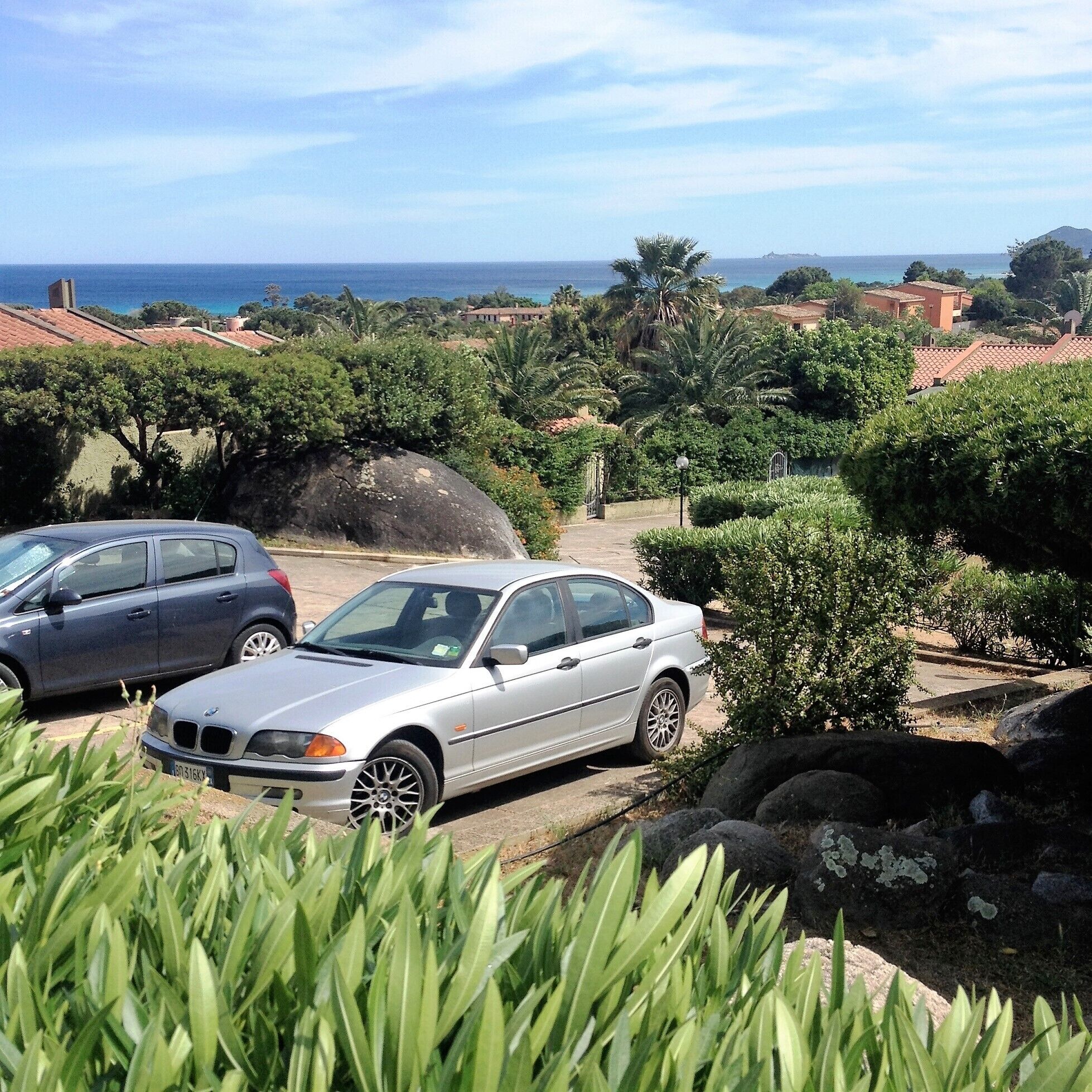 A silver BMW parked in a driveway with a view of the ocean and a coastal landscape.