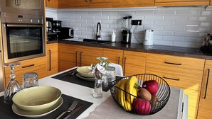 A modern kitchen with wooden cabinets, a built-in oven, a coffee maker, and a fruit bowl on the counter. - Fully equipped seafront house with spectacular seaview & small beach right below (Skiathos)