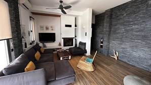 A modern living room with a dark grey sofa, a wooden coffee table, a wicker chair, a fireplace, and a flat-screen TV mounted on the wall. - Fully equipped seafront house with spectacular seaview & small beach right below (Skiathos)