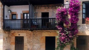 A building with a stone facade, a balcony with black railings, and potted plants with pink flowers.