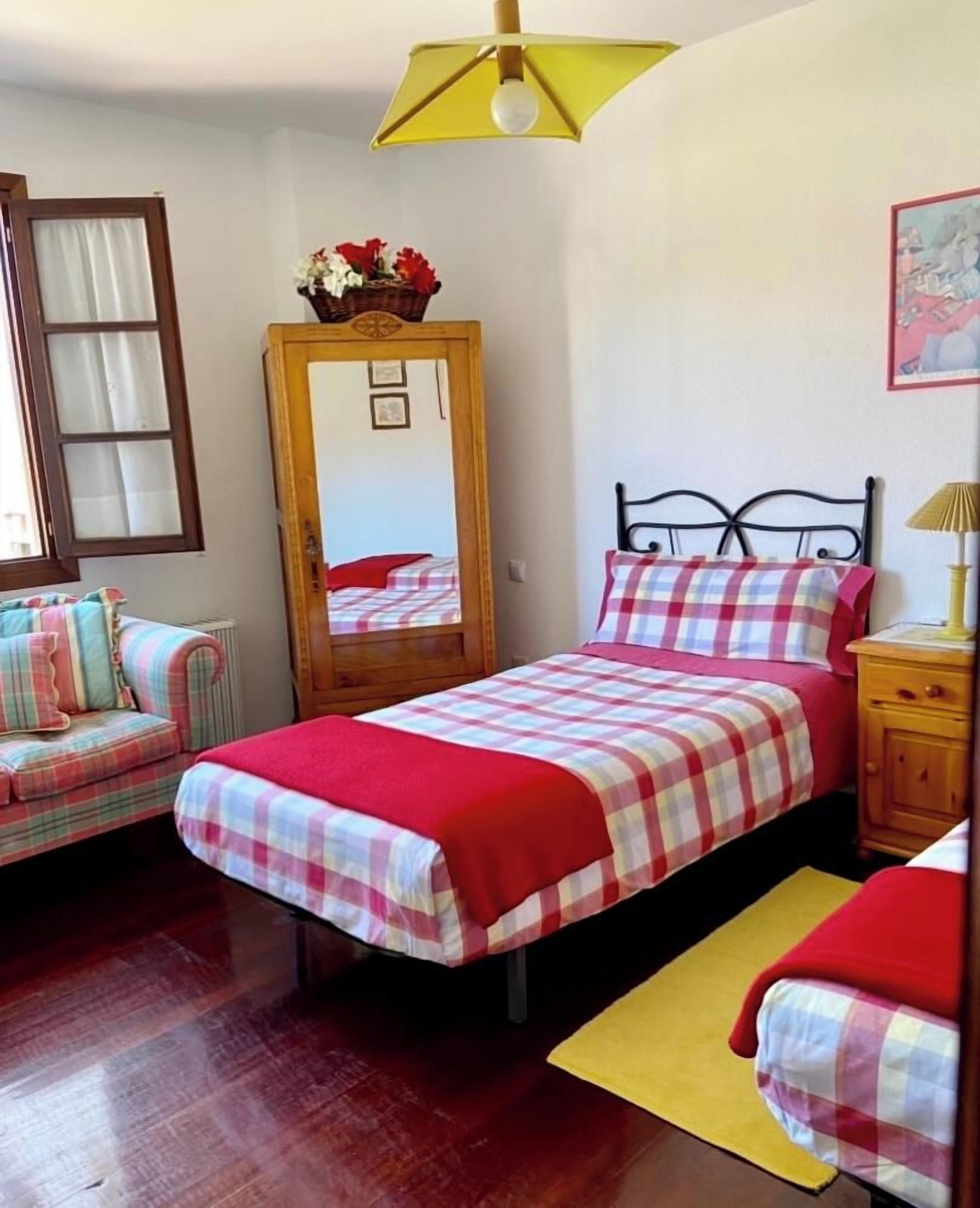 A bedroom with two beds, a wooden nightstand, a mirror, and a window with curtains.
