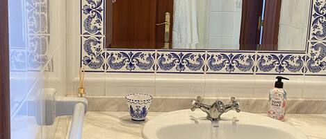 Ein Badezimmer mit einem weißen Waschbecken, blau-weißen Fliesen, einem Spiegel und einer Holztür.
