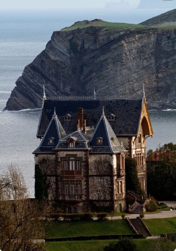 A historic building with a prominent tower, situated by a cliff overlooking the sea.
