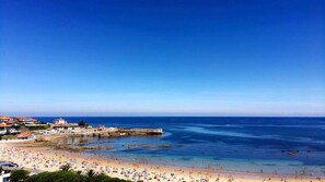 A coastal beach with a rocky breakwater, sandy shore, and buildings in the background.