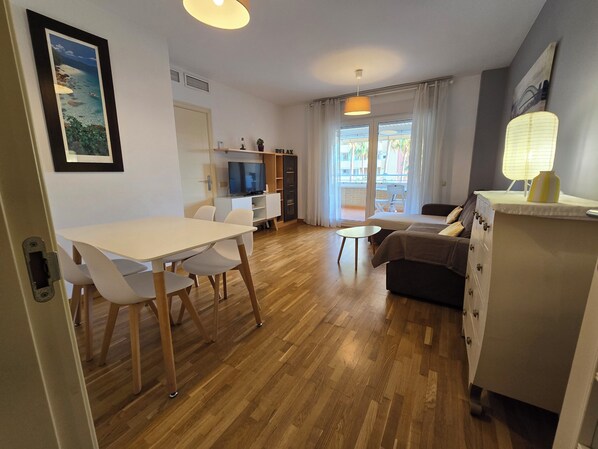Ein modernes Wohnzimmer mit einer Couch, einem Fernseher und einem Essbereich mit Tisch und Stühlen.