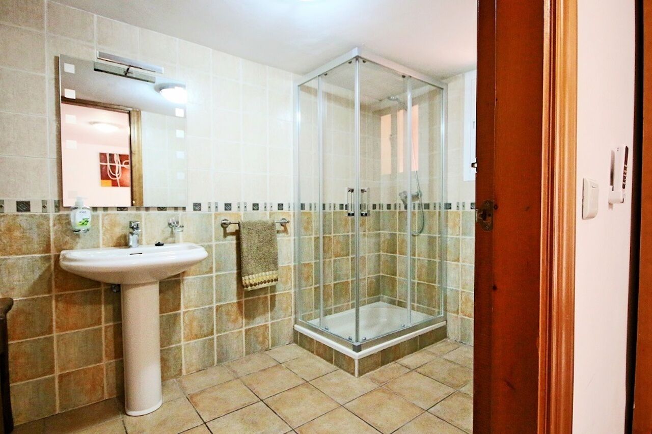 Een badkamer met een douchecabine van glas, een wastafel op een voetstuk en een betegelde vloer.