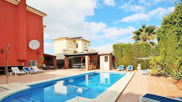 Une piscine avec des chaises longues, un bâtiment rouge et une maison à deux étages dotée d’une terrasse.