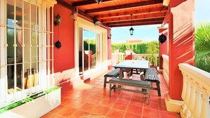 Une terrasse couverte avec un plafond en bois, une table et des bancs, et une vue sur la verdure.