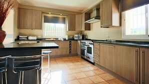 Une cuisine moderne avec des meubles en bois, un îlot central, des appareils électroménagers en acier inoxydable et une grande fenêtre qui laisse entrer la lumière naturelle.