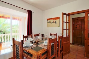 A dining area with a wooden table set for four, surrounded by chairs with woven seat backs.