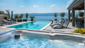 A swimming pool with lounge chairs and a hot tub, overlooking a body of water. - Luxury Villa POCRNJA with private heated pool, jacuzzi, sauna and pool table (Stanici)
