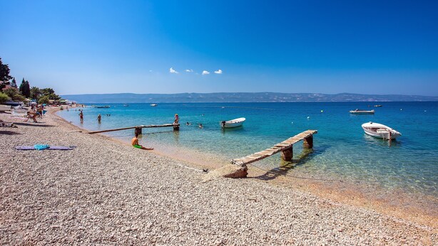 A pebbled beach with boats, a wooden pier, and clear blue water. - Luxury Villa POCRNJA with private heated pool, jacuzzi, sauna and pool table (Stanici)