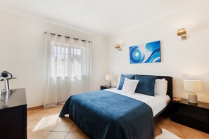Une chambre dâhĂŽtel avec un lit, deux tables de chevet avec des lampes, un tableau au mur et une fenĂȘtre avec des rideaux lĂ©gers.