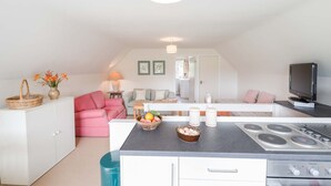 A compact kitchen with a central island, a dining area with a pink sofa, and a TV on the right.