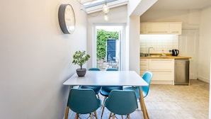 A modern kitchen with white cabinets, a sink, and a dishwasher. There is a dining area with a table and chairs, and a potted plant on the table.