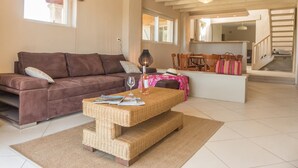 Un salon avec un canapé marron, une table basse en osier et un escalier menant à l’étage supérieur.