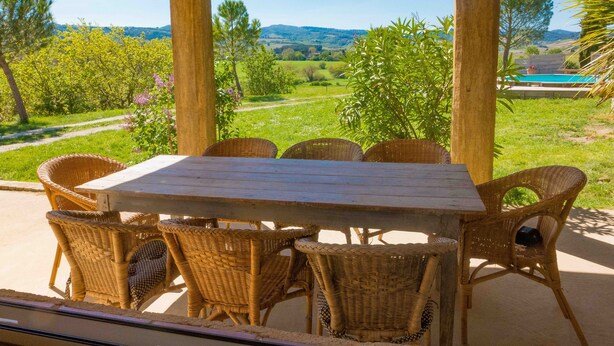 Un espace extérieur aménagé, abrité et doté de mobilier en osier, offrant une vue sur une piscine et un paysage verdoyant.