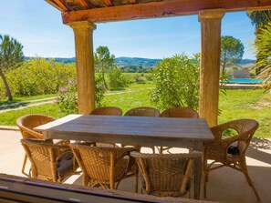 Un espace extérieur aménagé, abrité et doté de mobilier en osier, offrant une vue sur une piscine et un paysage verdoyant.