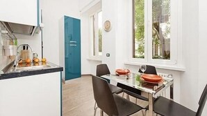 A modern kitchen with a built-in island, a dining area with a glass table and black chairs, and a view of greenery through a window. - New and comfortable apartment near the Vatican (Roma)