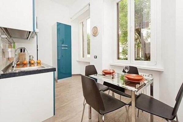 A modern kitchen with a built-in island, a dining area with a glass table and black chairs, and a view of greenery through a window. - New and comfortable apartment near the Vatican (Roma)