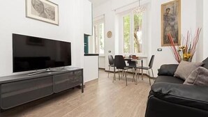 A modern living room with a flat-screen TV, a black sofa, and a dining area with chairs and a table. - New and comfortable apartment near the Vatican (Roma)