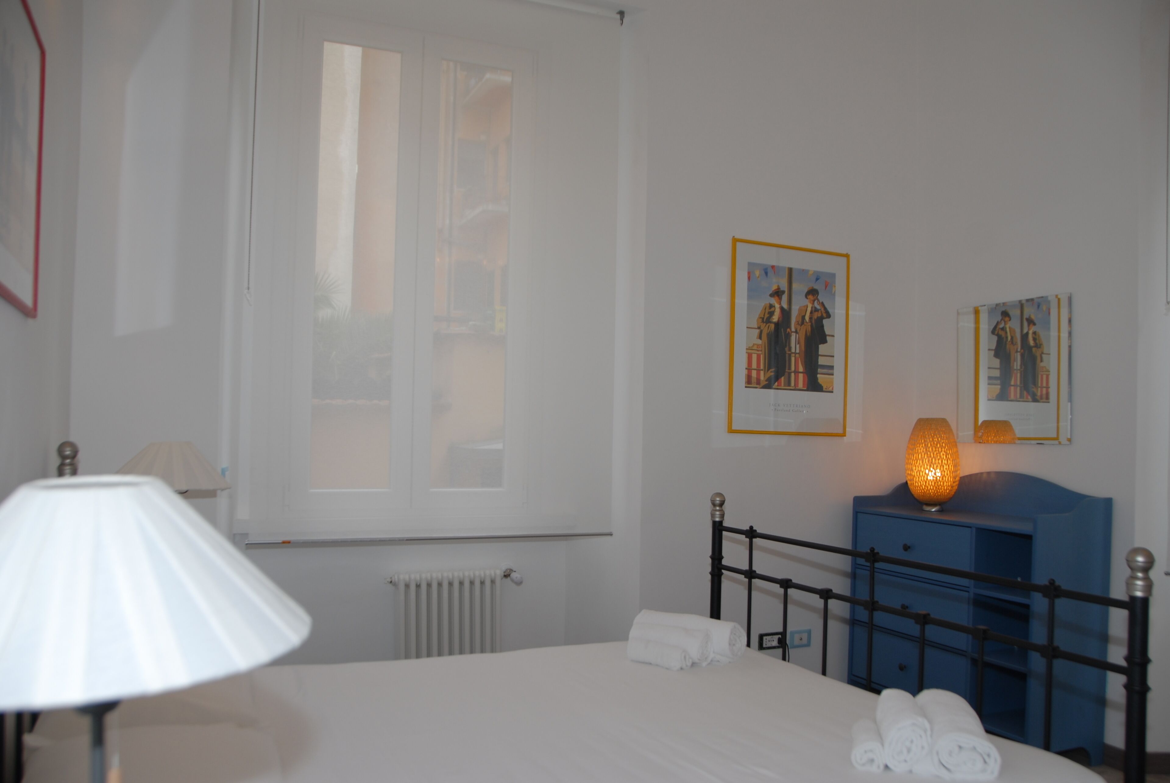 Habitación de hotel con una cama, una lámpara, un aparador y dos cuadros en la pared.