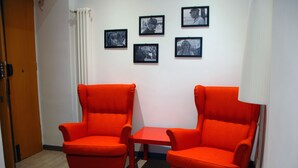 A room with two orange armchairs, a small table, and a white lamp. There are four framed pictures on the wall. - New and comfortable apartment near the Vatican (Roma)