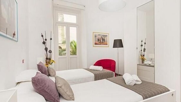 A hotel room with two beds, a red chair, a lamp, and a mirror. - New and comfortable apartment near the Vatican (Roma)