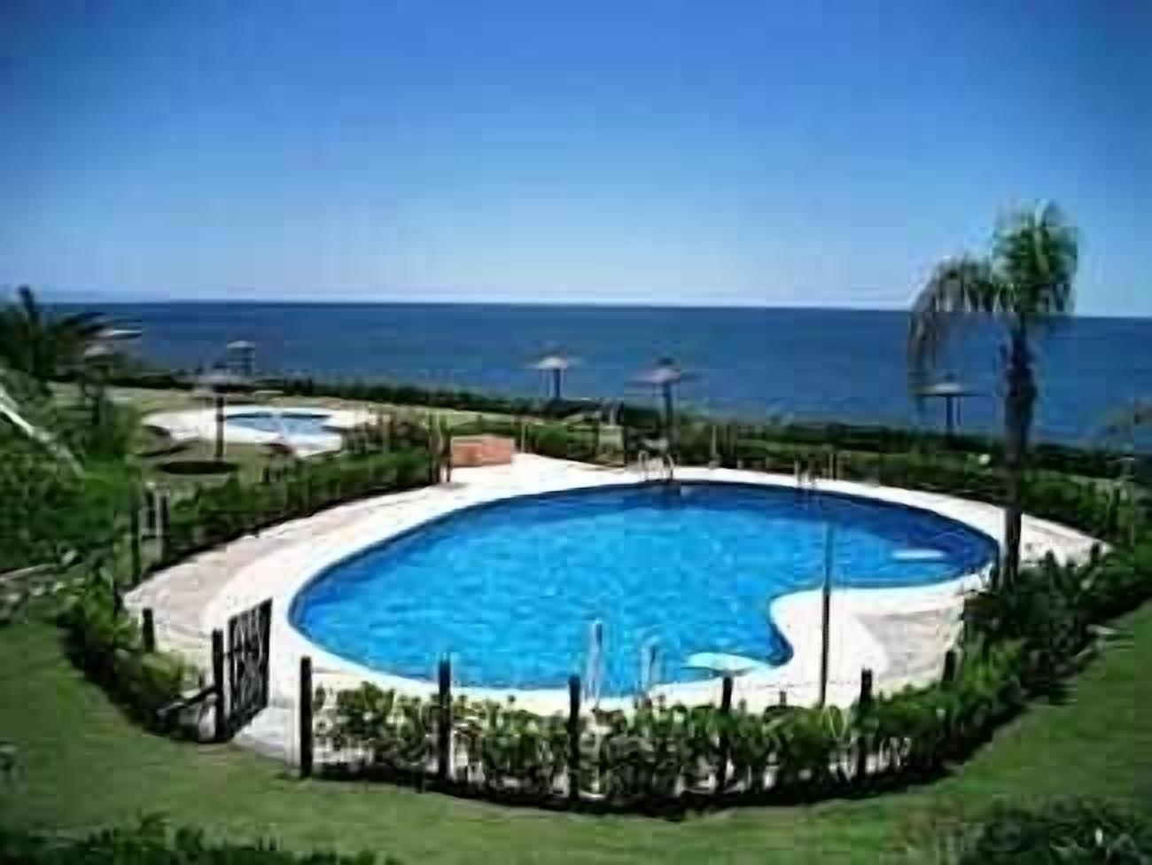 A swimming pool with a view of the ocean, surrounded by a fence and greenery.