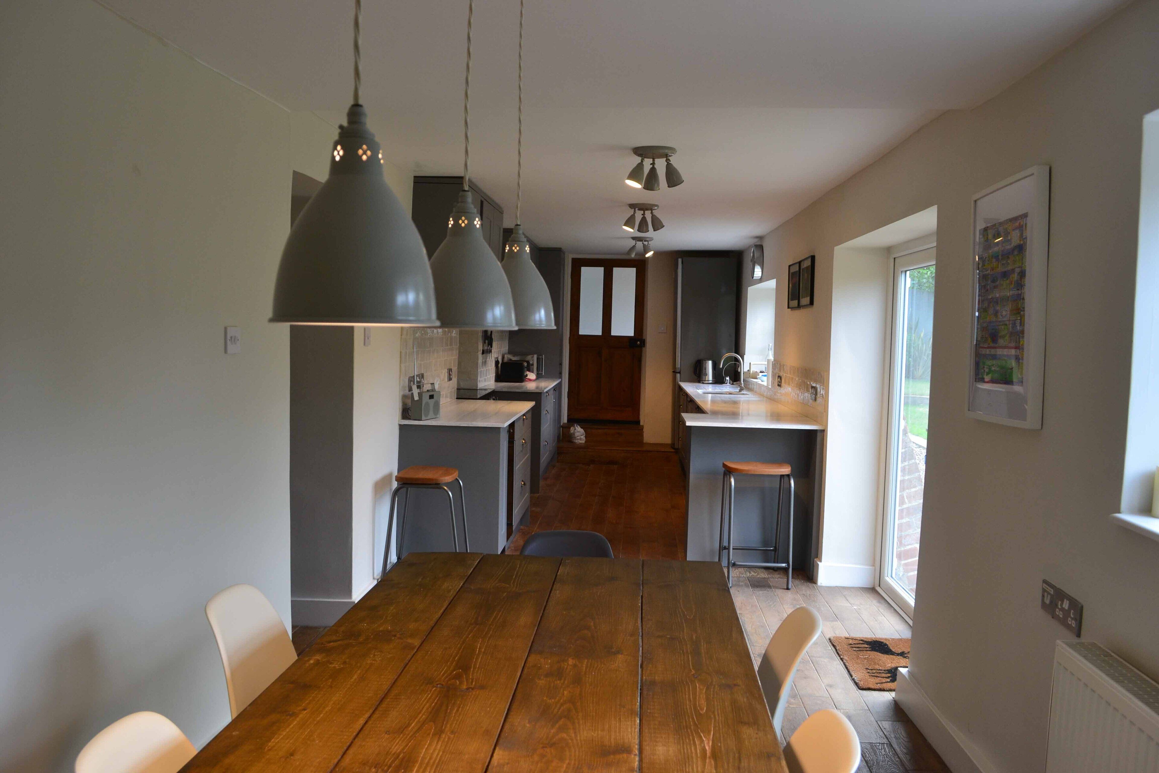 Une cuisine moderne avec des luminaires suspendus, une table à manger en bois et une vue sur l’espace repas.