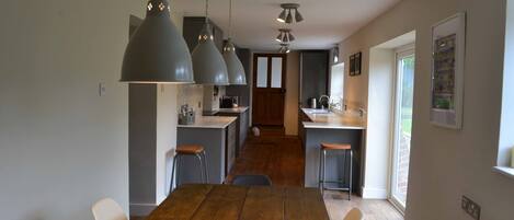 Une cuisine moderne avec des luminaires suspendus, une table à manger en bois et une vue sur l’espace repas.