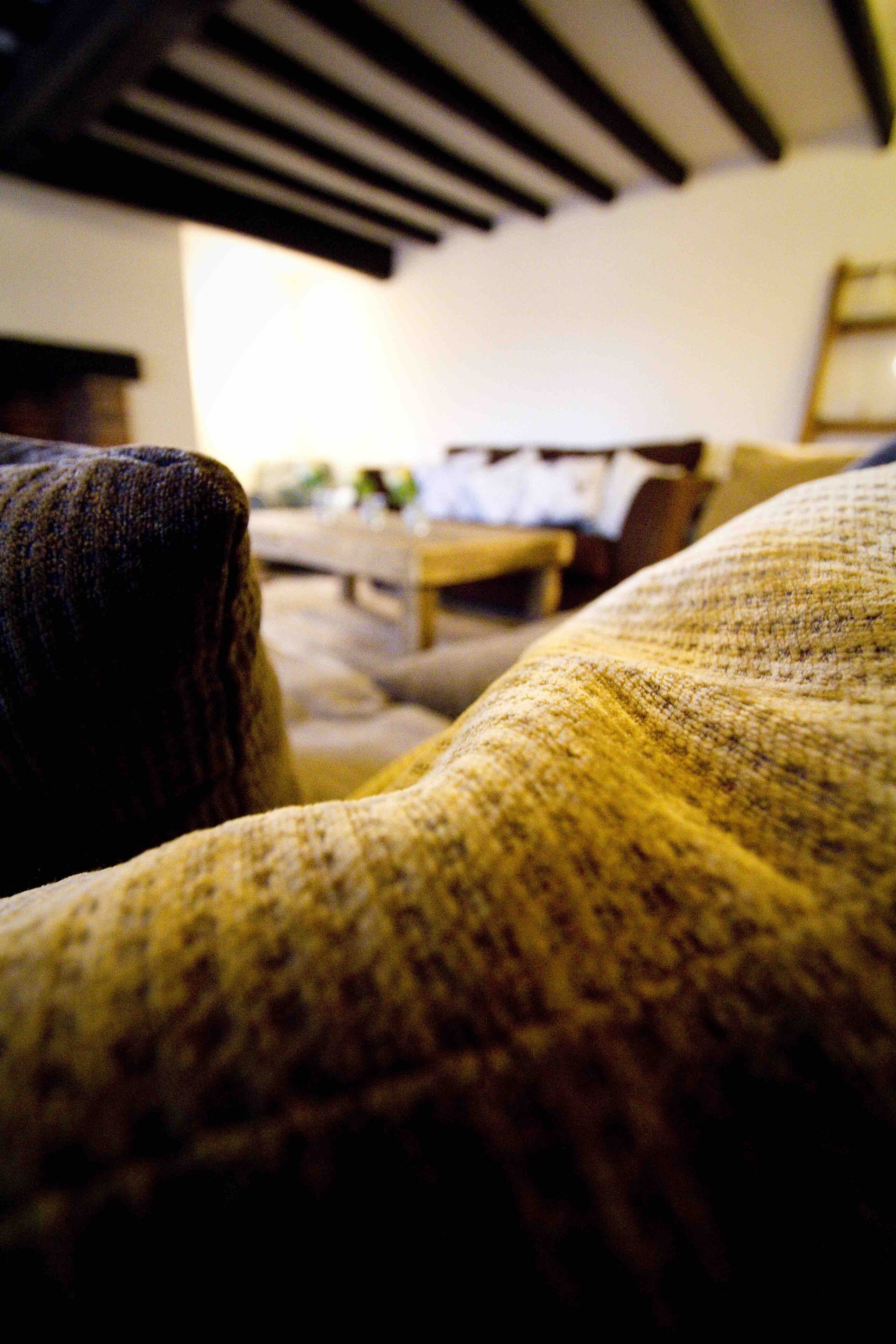 Ein Detailaufnahme eines strukturierten Stoffes, vermutlich eine Couch oder ein Sessel, in einem Raum mit schräg verlaufender Decke und einer sichtbaren Leuchte.