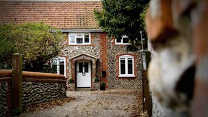 Un bâtiment en pierre avec un toit recouvert de tuiles, une porte blanche et un petit porche.