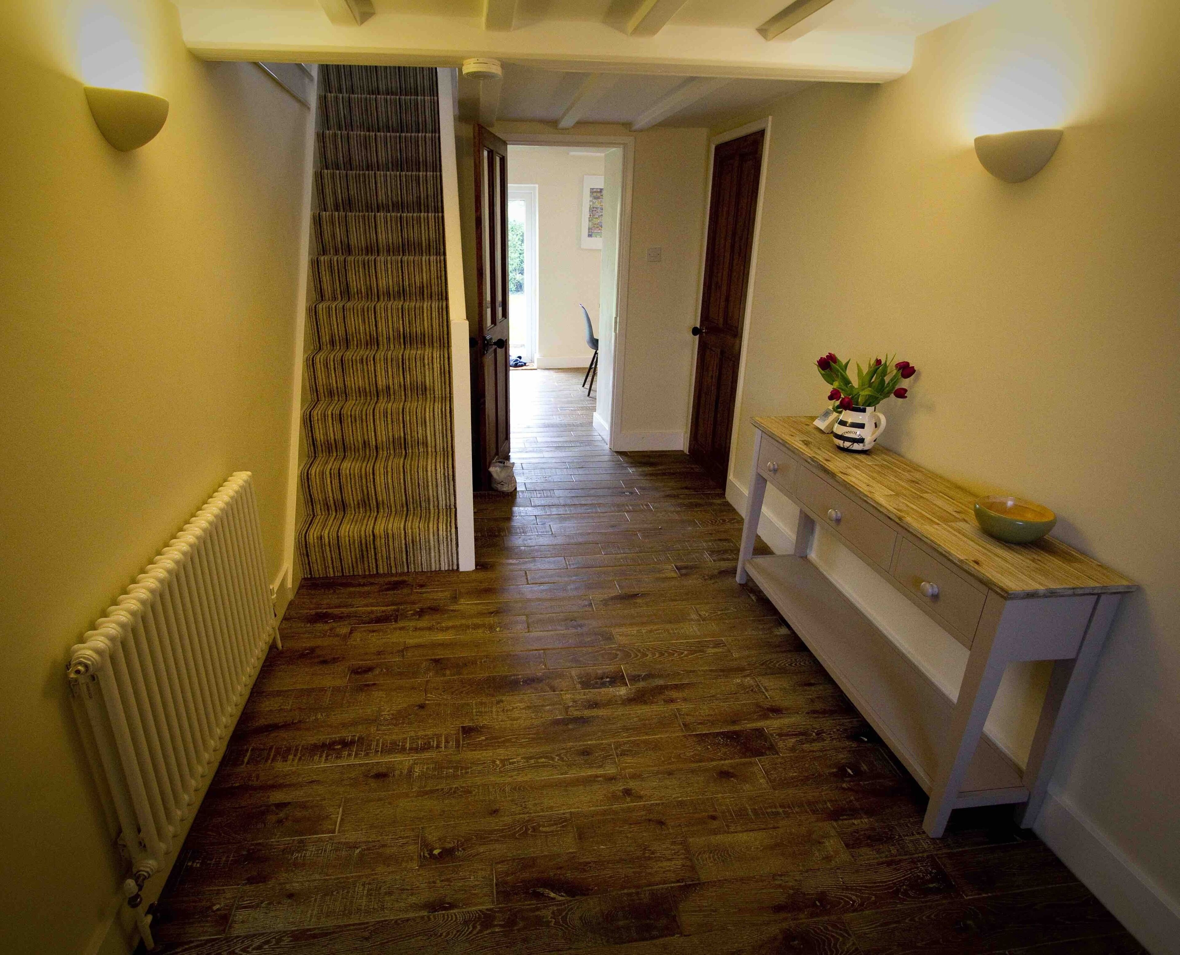 A hallway with wooden flooring, a radiator, a staircase, and a wooden console table with a vase of flowers.