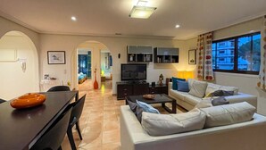 A modern living room with a sofa, TV, and dining area. - Apartamento T2, Praia da Falésia, Albufeira (Albufeira)
