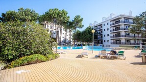 A pool area with lounge chairs, a clear blue pool, and a building with balconies in the background. - Apartamento T2, Praia da Falésia, Albufeira (Albufeira)