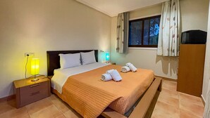 A hotel room with a bed, a nightstand with a lamp, a window with curtains, and a wooden wardrobe. - Apartamento T2, Praia da Falésia, Albufeira (Albufeira)