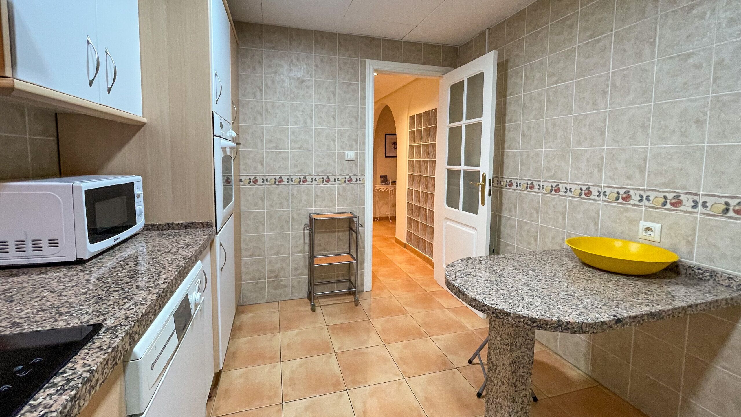 Una cocina con microondas, un lavabo con un recipiente amarillo y salpicadero de azulejos.