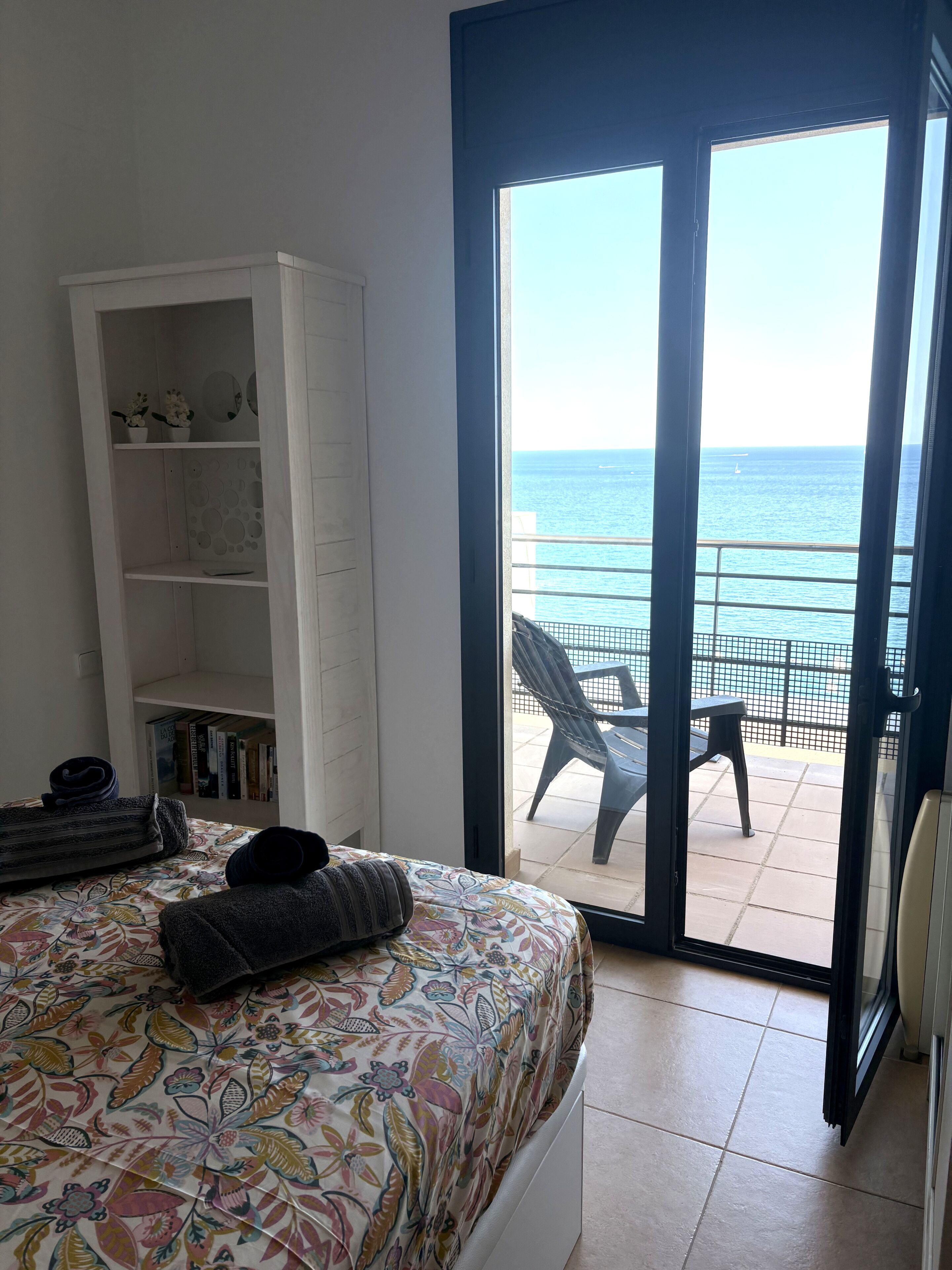 Une chambre à coucher avec un lit, une armoire et une vue sur la mer, accessible par une porte coulissante.