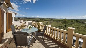 A balcony with a table and chairs, offering a view of a green landscape and distant hills. - Sol y Campo (with wifi) 10 min from the beach (Ariany)