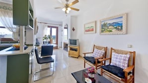A living room with a TV, two wooden chairs, a coffee table, and a ceiling fan. - Sol y Campo (with wifi) 10 min from the beach (Ariany)