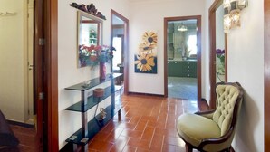 A hallway with a glass display cabinet, a large floral painting, and a classic armchair. - Sol y Campo (with wifi) 10 min from the beach (Ariany)