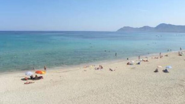 A beach with clear turquoise water, people sunbathing, and a mountain in the background. - Sol y Campo (with wifi) 10 min from the beach (Ariany)