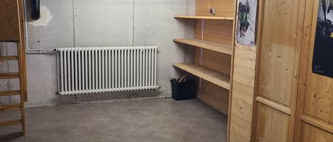 Ein Kellerraum mit Betonboden, einem Heizkörper, Holzregalen und einer Leiter.
