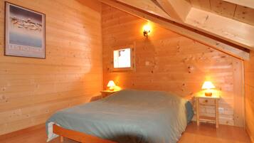 Une chambre à coucher dans une cabane en bois, avec un lit, deux tables de chevet avec des lampes, une affiche au mur et une fenêtre.