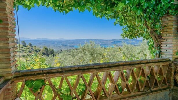 Un balcon donnant sur un paysage vallonné, avec un mur en briques et une clôture en treillis.