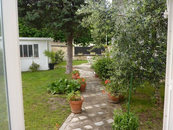 A stone pathway leading through a garden with potted plants and a white building in the background.