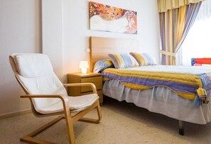 A bedroom with a bed, a chair, a nightstand, a lamp, and a painting on the wall.