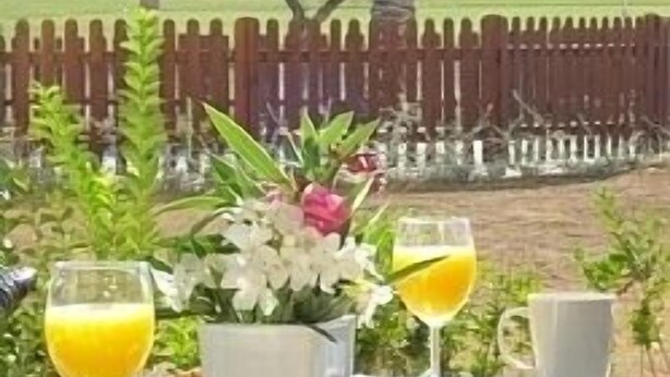 Mesa de comedor al aire libre con alimentos para el desayuno, una bebida y vistas de un edificio blanco con balcones.
