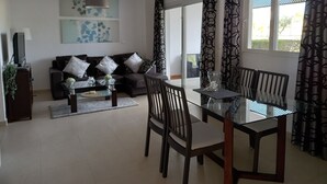 Una sala de estar moderna con una mesa de comedor de vidrio, sofás oscuros y cortinas estampadas.